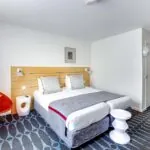 Chambre Familiale Supérieure avec deux lits et une chaise rouge à l’Hôtel Lorette