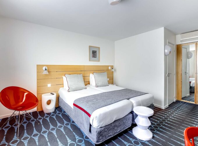 Chambre Familiale Supérieure avec deux lits et une chaise rouge à l’Hôtel Lorette