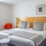 Chambre Twin Supérieure avec deux lits et une chaise rouge à l’Hôtel Lorette