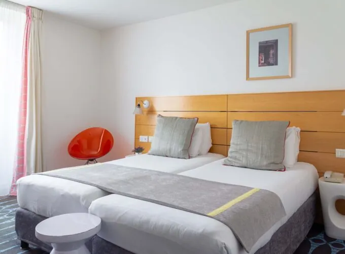 Chambre Twin Supérieure avec deux lits et une chaise rouge à l’Hôtel Lorette