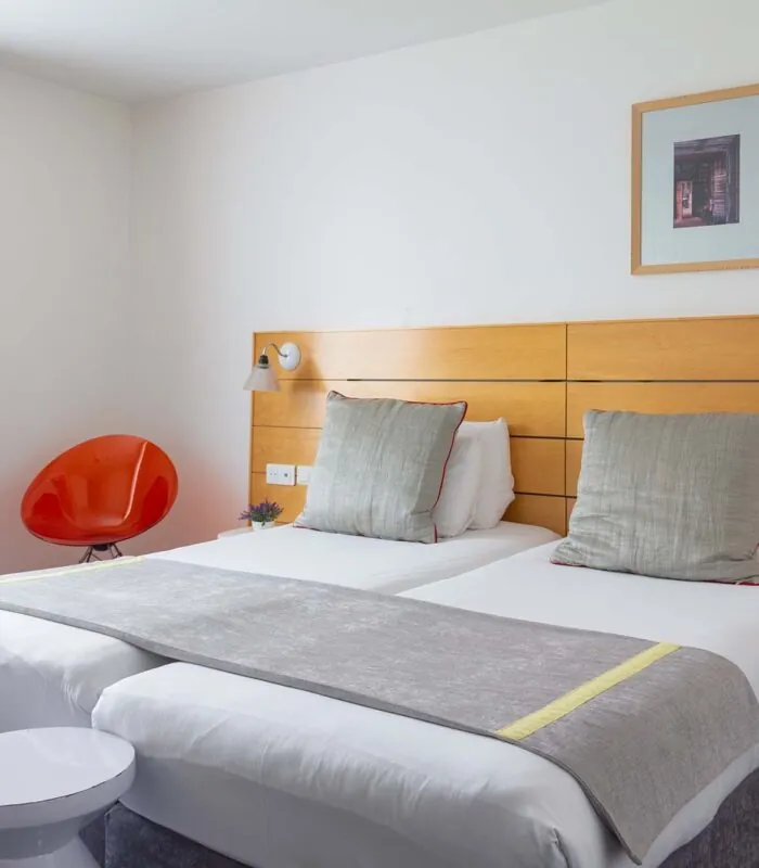Chambre Twin Supérieure avec deux lits et une chaise rouge à l’Hôtel Lorette