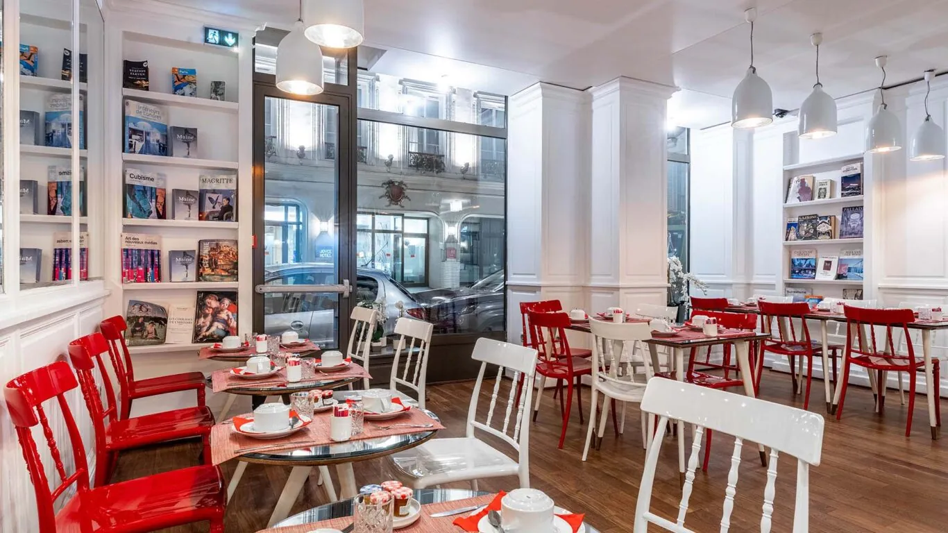 Salle de petit-déjeuner de l’hôtel 3 étoiles Monterosa du groupe Astotel à Paris, avec des chaises rouges et blanches, des tables en bois et une décoration murale sur le thème des livres