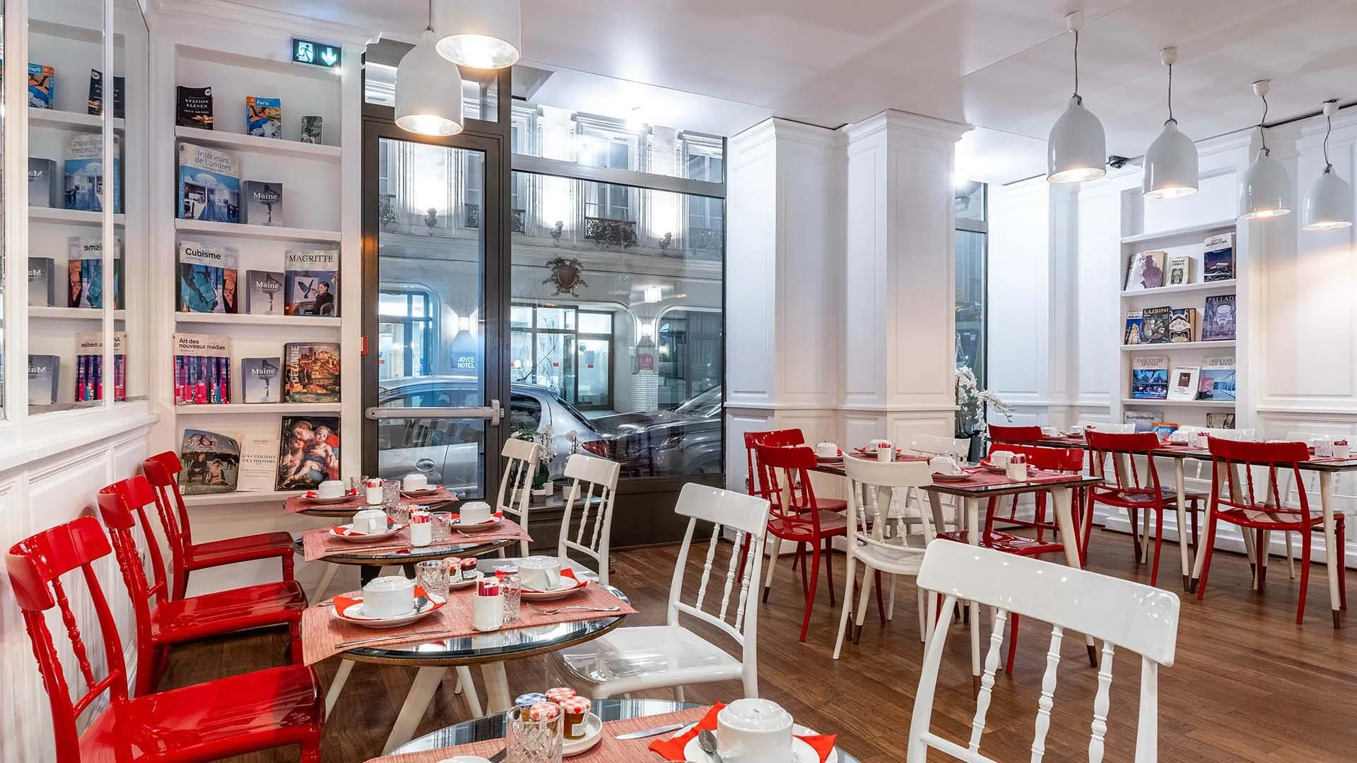 Salle de petit-déjeuner de l’hôtel 3 étoiles Monterosa du groupe Astotel à Paris, avec des chaises rouges et blanches, des tables en bois et une décoration murale sur le thème des livres