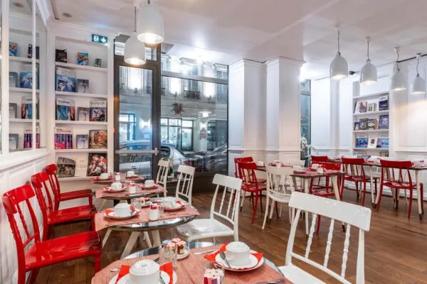 Salle de petit-déjeuner de l’hôtel 3 étoiles Monterosa du groupe Astotel à Paris, avec des chaises rouges et blanches, des tables en bois et une décoration murale sur le thème des livres