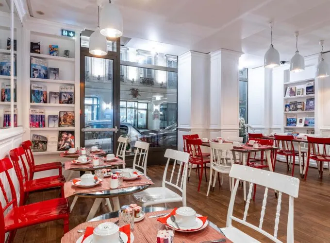 Salle de petit-déjeuner de l’hôtel 3 étoiles Monterosa du groupe Astotel à Paris, avec des chaises rouges et blanches, des tables en bois et une décoration murale sur le thème des livres