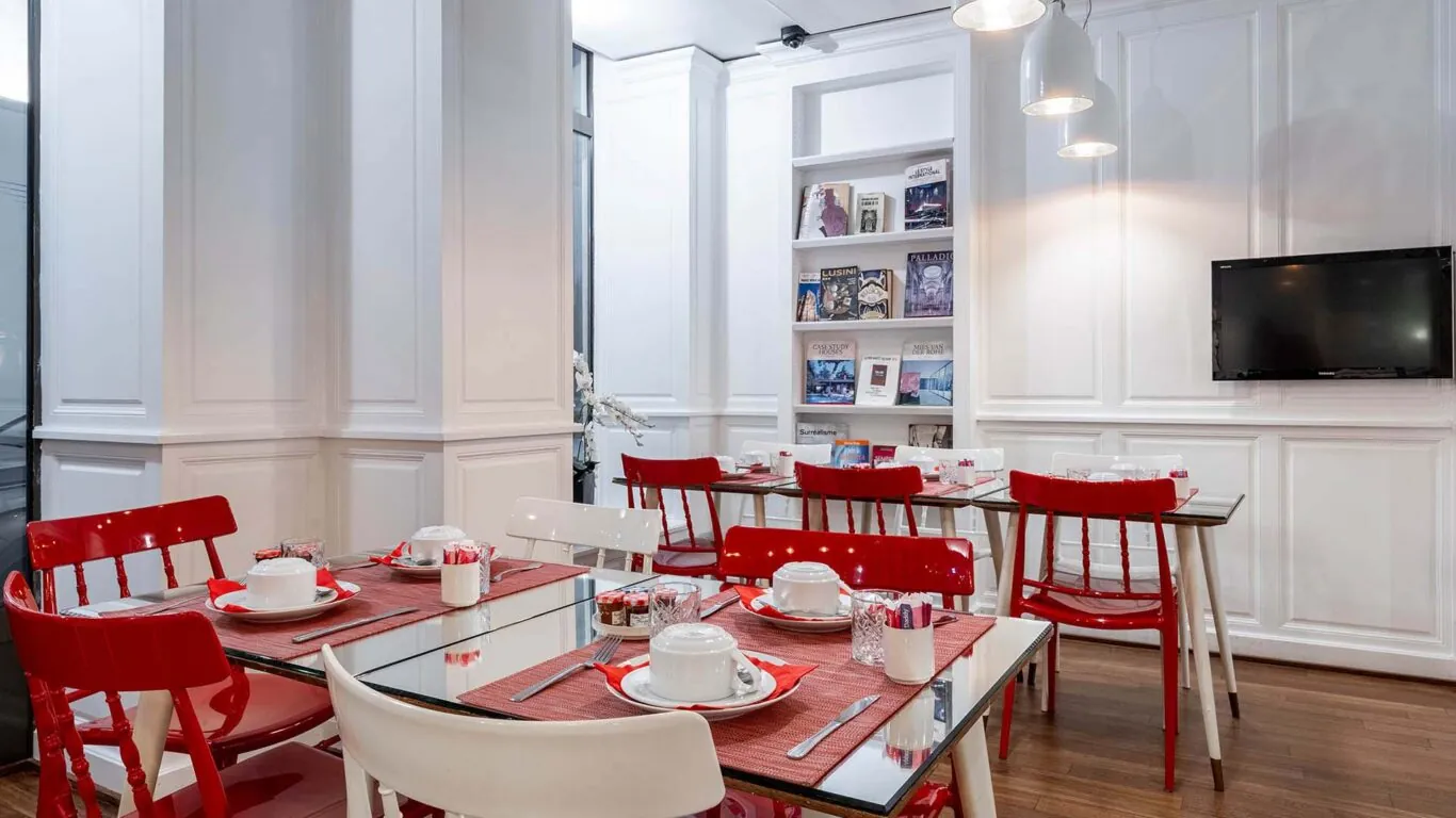Salle de petit-déjeuner de l’hôtel 3 étoiles Monterosa du groupe Astotel à Paris, avec des chaises rouges et blanches, des tables en bois et une décoration murale sur le thème des livres