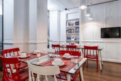 Salle de petit-déjeuner de l’hôtel 3 étoiles Monterosa du groupe Astotel à Paris, avec des chaises rouges et blanches, des tables en bois et une décoration murale sur le thème des livres