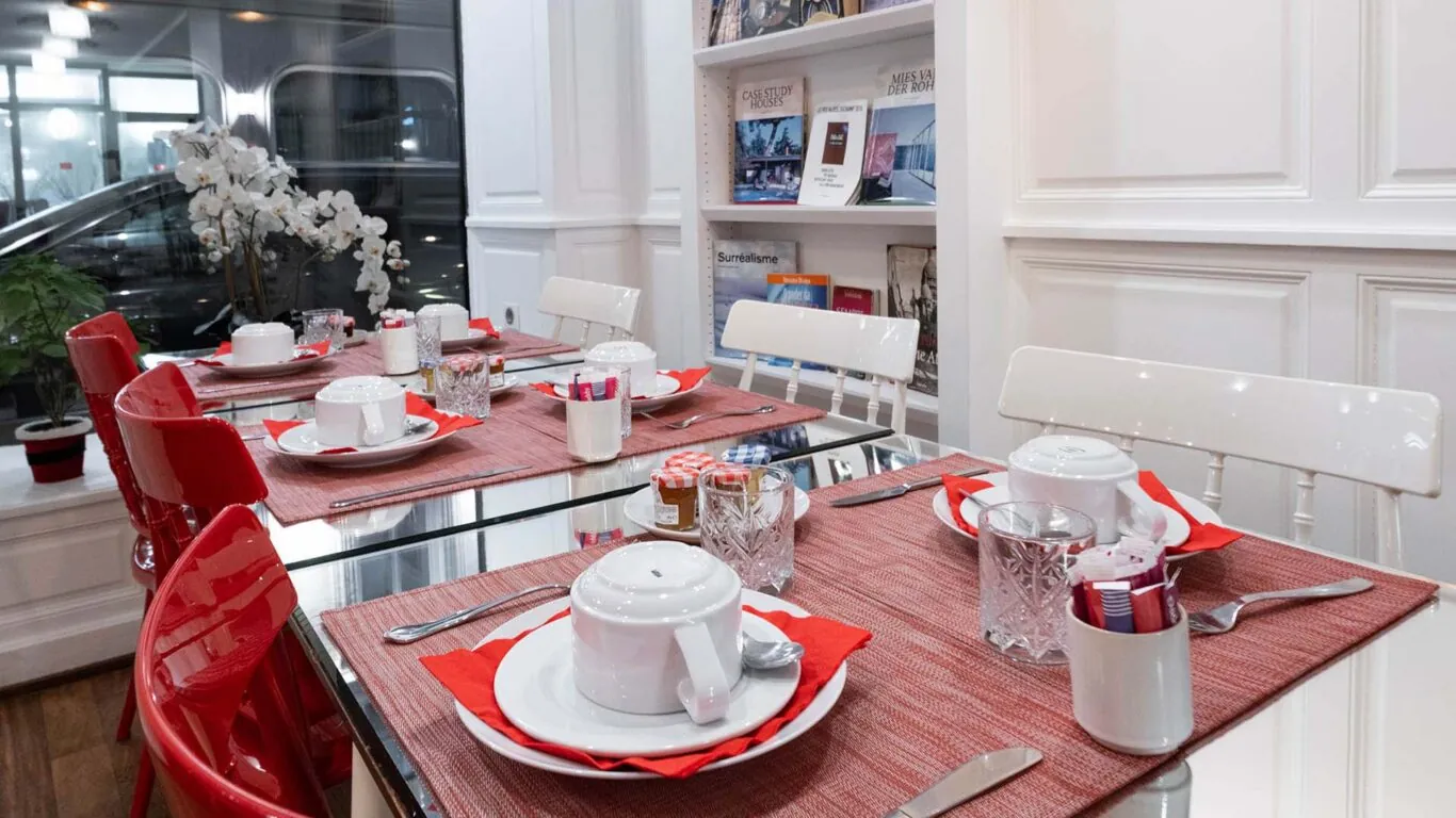 Salle de petit-déjeuner de l’hôtel 3 étoiles Monterosa du groupe Astotel à Paris, avec des chaises rouges et blanches, des tables en bois et une décoration murale sur le thème des livres