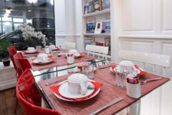 Salle de petit-déjeuner de l’hôtel 3 étoiles Monterosa du groupe Astotel à Paris, avec des chaises rouges et blanches, des tables en bois et une décoration murale sur le thème des livres