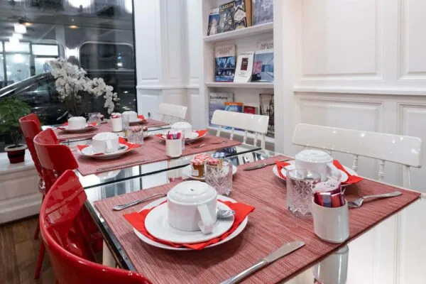 Salle de petit-déjeuner de l’hôtel 3 étoiles Monterosa du groupe Astotel à Paris, avec des chaises rouges et blanches, des tables en bois et une décoration murale sur le thème des livres