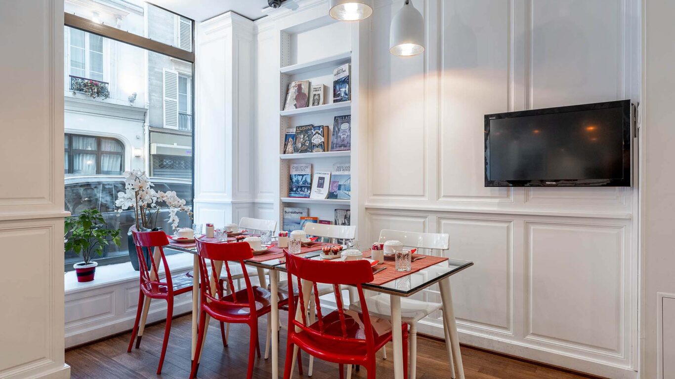 Salle de petit-déjeuner de l’hôtel 3 étoiles Monterosa du groupe Astotel à Paris, avec des chaises rouges et blanches, des tables en bois et une décoration murale sur le thème des livres
