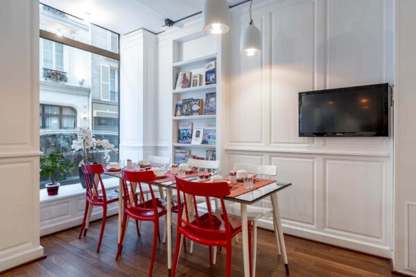 Salle de petit-déjeuner de l’hôtel 3 étoiles Monterosa du groupe Astotel à Paris, avec des chaises rouges et blanches, des tables en bois et une décoration murale sur le thème des livres