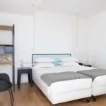 Une des 2 chambres de la chambre communicante avec deux lits et une chaise à l’Hôtel Palm