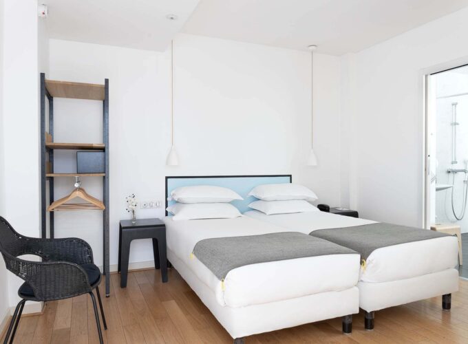 Une des 2 chambres de la chambre communicante avec deux lits et une chaise à l’Hôtel Palm