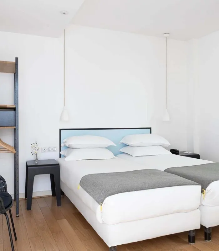 Une des 2 chambres de la chambre communicante avec deux lits et une chaise à l’Hôtel Palm