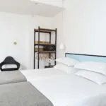 Une des 2 chambres de la chambre Communicante avec deux lits et une chaise en bois à l’Hôtel Palm