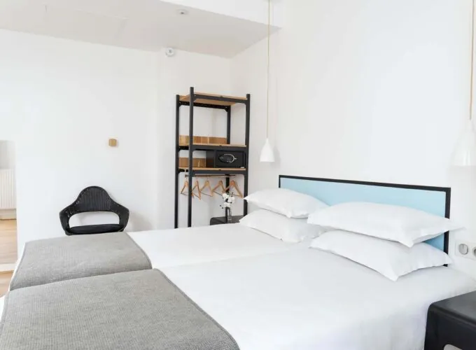 Une des 2 chambres de la chambre Communicante avec deux lits et une chaise en bois à l’Hôtel Palm
