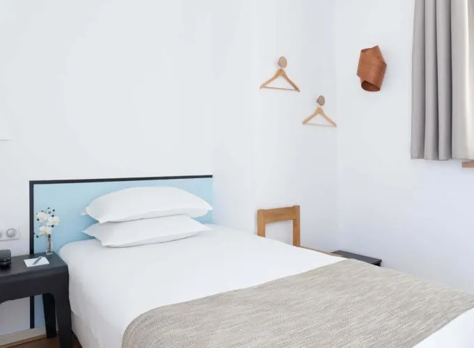 Une des 2 chambres de la chambre communicante avec un lit simple et une tête de lit bleue à l’Hôtel Palm