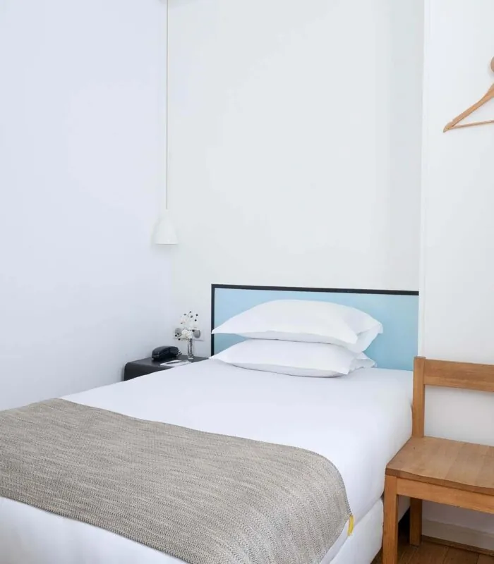 Une des 2 chambres de la chambre communicante avec un lit simple et deux cintres au mur à l’Hôtel Palm