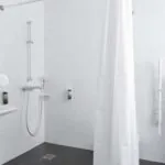 Salle de bain d’une des 2 chambres de la chambre communicante avec un rideau de douche blanc et un lavabo à l’Hôtel Palm