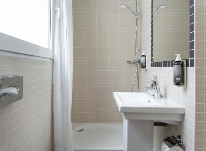 Salle de bain d’une des 2 chambres de la chambre communicante avec un lavabo, un miroir et une douche à l’Hôtel Palm