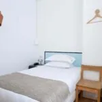 Chambre de la chambre Single Cocoon avec un lit simple et deux cintres au mur à l’Hôtel Palm