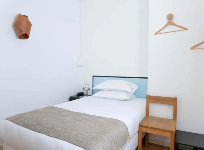 Chambre de la chambre Single Cocoon avec un lit simple et deux cintres au mur à l’Hôtel Palm