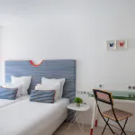 Chambre Twin lumineuse à l’Hôtel 34B avec deux lits simples, tête de lit rayée, bureau et télévision.