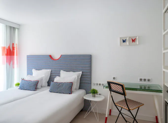 Chambre Twin lumineuse à l’Hôtel 34B avec deux lits simples, tête de lit rayée, bureau et télévision.