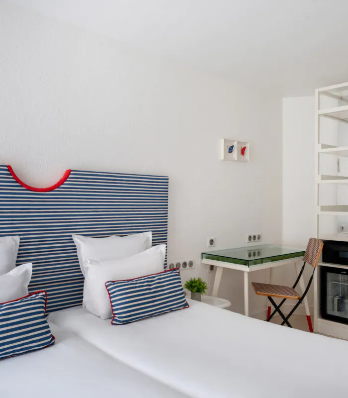Chambre Twin lumineuse à l’Hôtel 34B avec deux lits simples, tête de lit rayée, bureau et télévision.