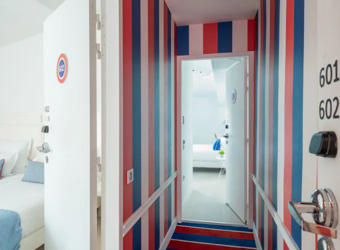 Couloir de la Chambre Familiale avec des rayures rouges, blanches et bleues et le numéro 601 sur la porte à l’Hôtel 34B