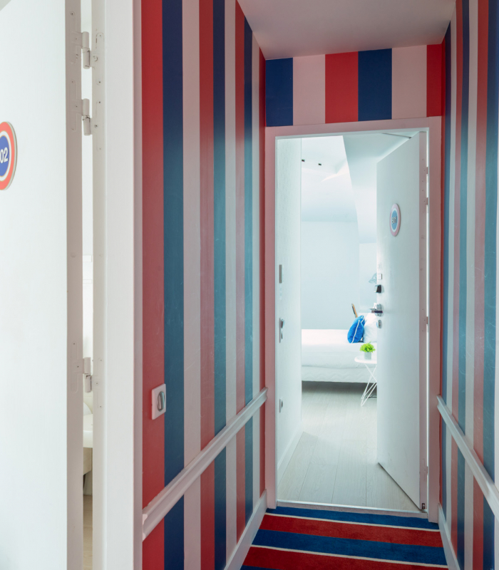 Couloir de la Chambre Familiale avec des rayures rouges, blanches et bleues et le numéro 601 sur la porte à l’Hôtel 34B