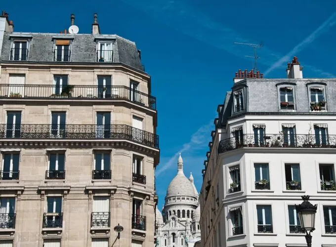 Façades haussmanniennes à Pigalle avec vue sur la basilique du Sacré-Cœur de Montmartre sous un ciel bleu à Paris.