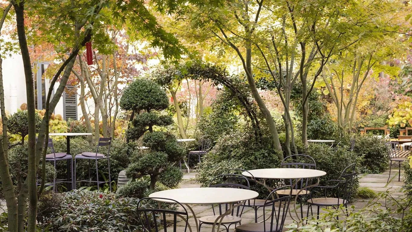 Jardin paisible de l’hôtel Regent’s Garden à Paris, avec des tables et des chaises entourées de verdure et d’arbres taillés