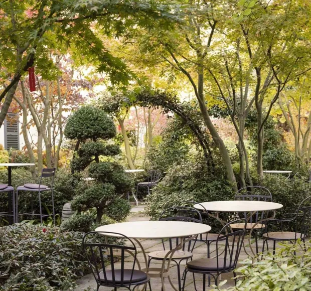 Giardino tranquillo dell’Hotel Regent’s Garden a Parigi, con tavoli e sedie circondati da verde e alberi potati