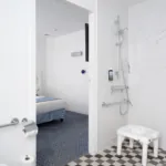 salle de bain accessible avec douche à l’italienne, siège, barres d’appui et vue sur la chambre à l’hôtel 34b