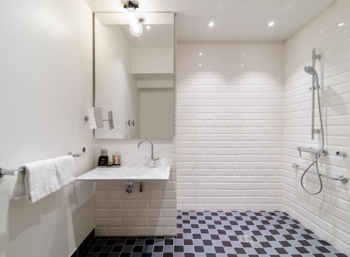 salle de bain accessible avec douche à l’italienne, siège, barres d’appui et lavabo adapté à l’hôtel 34b