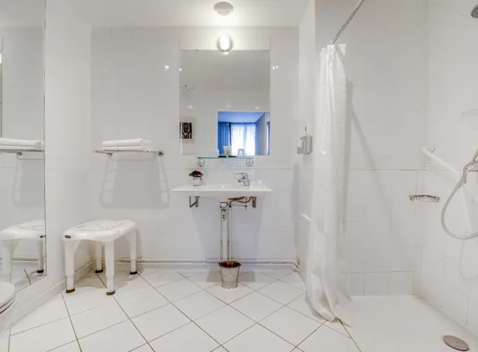 salle de bain accessible avec douche à l’italienne, siège et lavabo à l’hôtel lorette