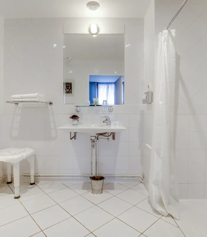 salle de bain accessible avec douche à l’italienne, siège et lavabo à l’hôtel lorette