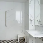 salle de bain accessible avec douche à l’italienne, siège, barres d’appui et vue sur la chambre à l’hôtel 34b
