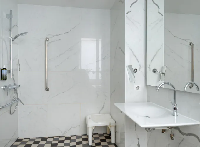 salle de bain accessible avec douche à l’italienne, siège, barres d’appui et vue sur la chambre à l’hôtel 34b