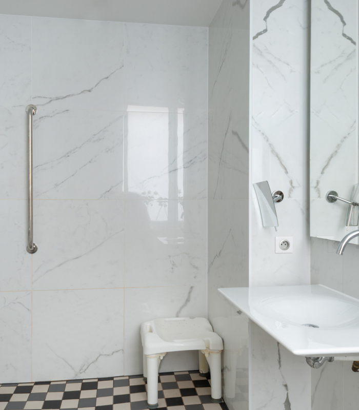 salle de bain accessible avec douche à l’italienne, siège, barres d’appui et vue sur la chambre à l’hôtel 34b