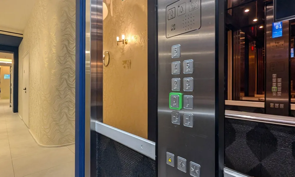 Innenansicht des barrierefreien Aufzugs im Hotel Astra Opéra in Paris mit Bedienfeld mit Braille- und Großschrift-Tasten, Spiegel, Handlauf sowie visuellen und akustischen Signalen.