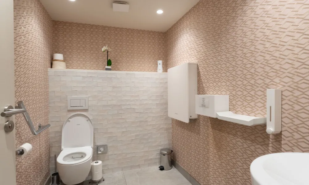 Barrierefreie Toilette des Hotel Astra Opéra in Paris, im ersten Untergeschoss gelegen, mit Haltegriffen, Wickeltisch und Waschbecken für Personen mit eingeschränkter Mobilität.