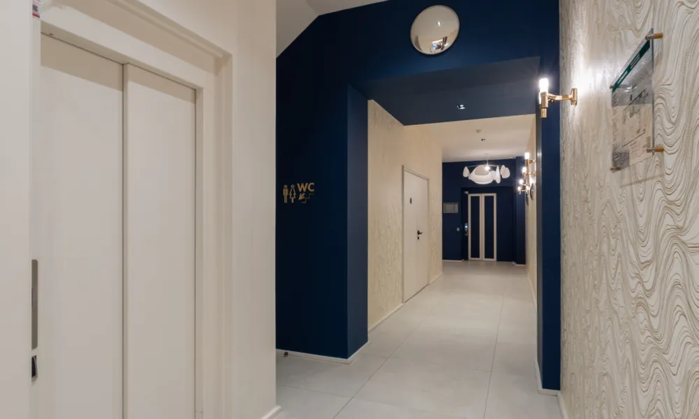 Heller Korridor des Hotel Astra Opéra in Paris mit Aufzügen, blauen Wänden und Wandbeleuchtung, der Zugang zu Gästeservices wie Gepäckaufbewahrung und kostenlosem WLAN bietet.