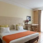 Chambre Familiale Privilège à l’hôtel Le 123 Elysées avec un grand lit, des oreillers jaunes et blancs et un bureau