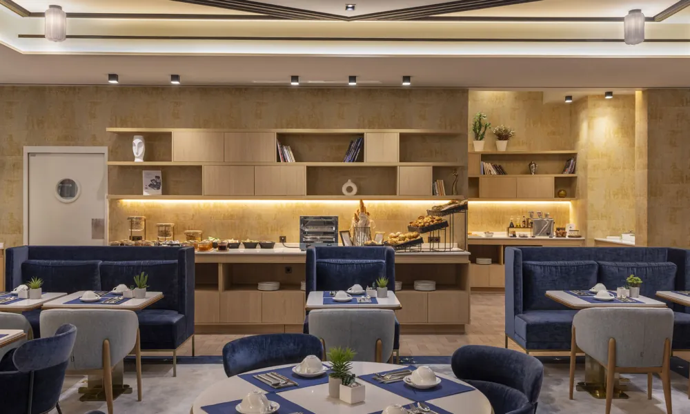 Speisesaal in Paris mit runden Tischen, blauen Stühlen, Selbstbedienungsbuffet und Einrichtungen, die für alle Gäste geeignet sind.