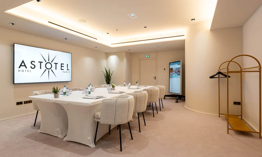 Besprechungsraum des Hotel Astra Opéra in Paris mit großem weißen Tisch, bequemen Stühlen, Präsentationsbildschirm, einstellbarer Beleuchtung und großzügigem, freiem Bewegungsraum.