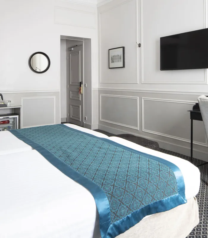 Lits d’une Chambre Twin Privilège à l’Hôtel Bradford Elysées avec draps blancs et chemin de lit bleu
