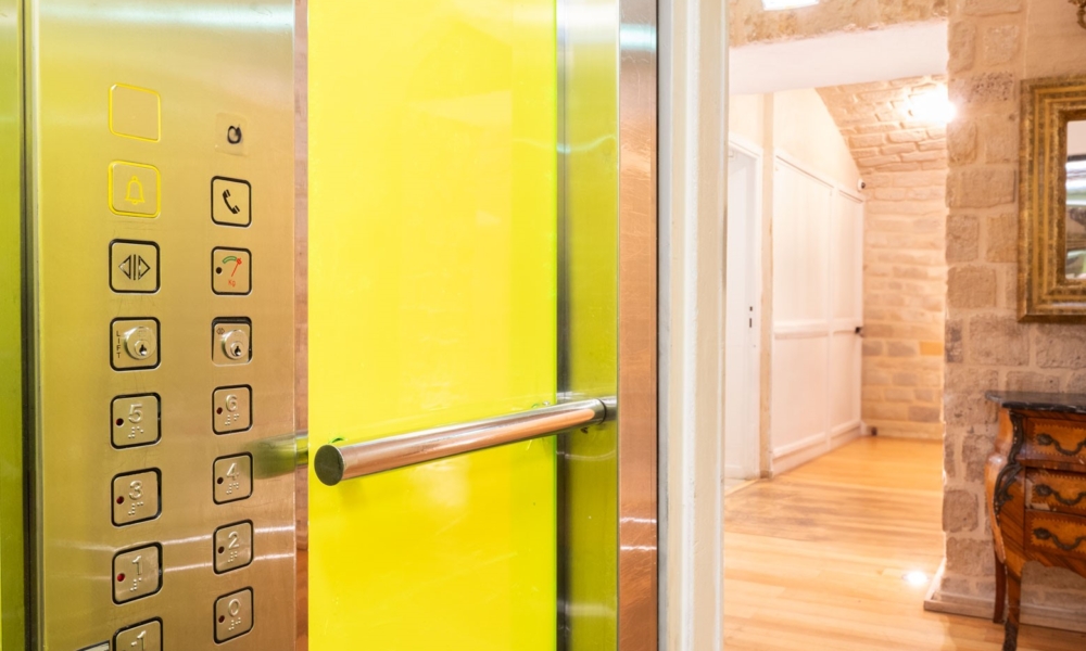 Elevador acessível do Hotel Lorette – Astotel, equipado com corrimão e painel de botões visível.